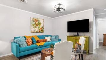 A living room with a blue sofa, a television, a green cabinet, and a patterned rug.