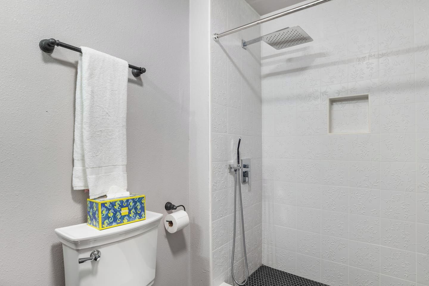 Une salle de bain équipée d’un WC, d’un porte-serviettes, d’une douche et d’un support à papier toilette.