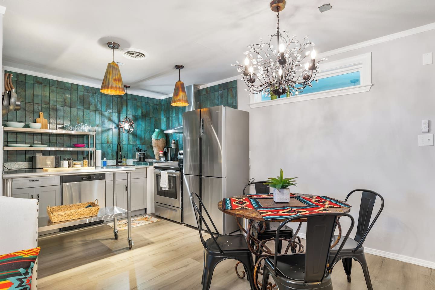 A modern kitchen with stainless steel appliances, a dining area with a patterned tablecloth, and a chandelier.