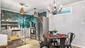 A modern kitchen with stainless steel appliances, a dining area with a patterned tablecloth, and a chandelier.