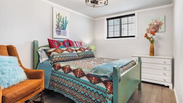 Una camera da letto con un letto, una sedia, una cassettiera e opere d'arte alle pareti.