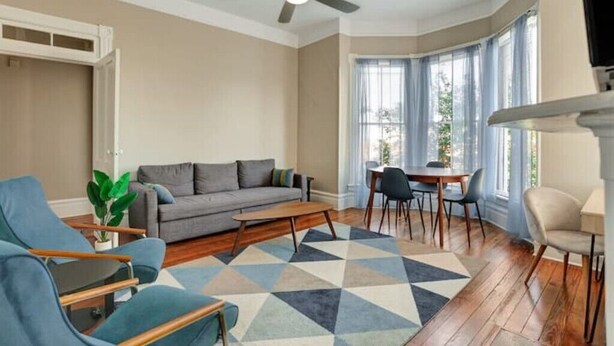 Un salon avec un canapé gris, des fauteuils bleus, une table basse en bois et un tapis à motifs.