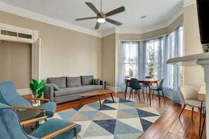 Un salon avec un canapé gris, des fauteuils bleus, une table basse en bois et un tapis à motifs.