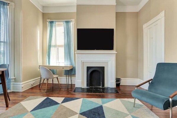 Un salon avec une cheminée, un téléviseur, un fauteuil bleu et un coin repas comprenant une table et des chaises.