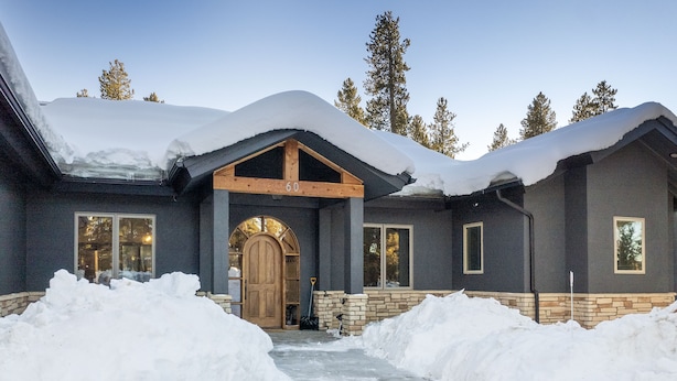 Una grande casa con facciata scura, una porta d'ingresso in legno e un tetto coperto di neve.