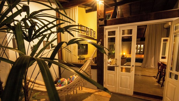 A room with a hammock, a dining area, and a view of the outside. - O Vilarejo Hospedaria e Gastronomia (Florianópolis)