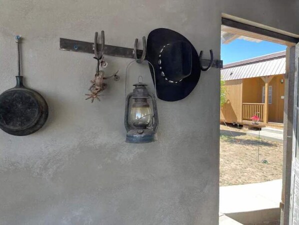 A rustic interior with a metal wall-mounted rack holding a frying pan, a lantern, and a cowboy hat. - Vibes Cowboy: Rhinestone Cowboy (Marfa)
