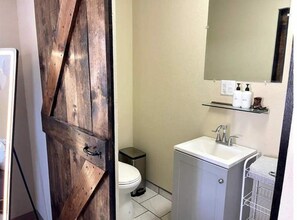 A bathroom with a wooden door, a toilet, a sink, and a mirror. - Vibes Cowboy: Rhinestone Cowboy (Marfa)