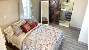 Een slaapkamer met een bed, een schuifdeur in boerderijstijl, een badkamer met wastafel en spiegel, en een airconditioner.