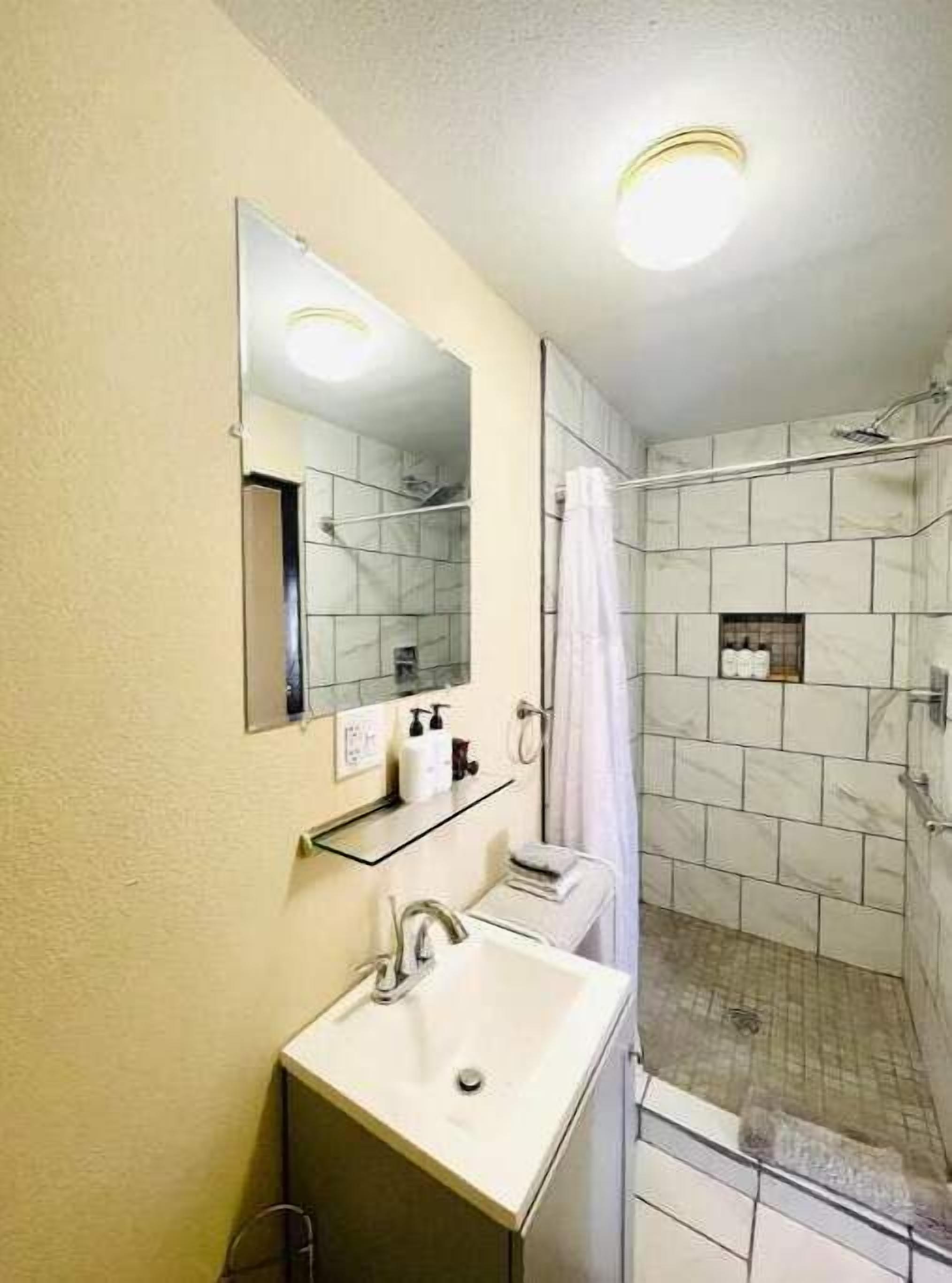 A bathroom with a sink, mirror, and shower.