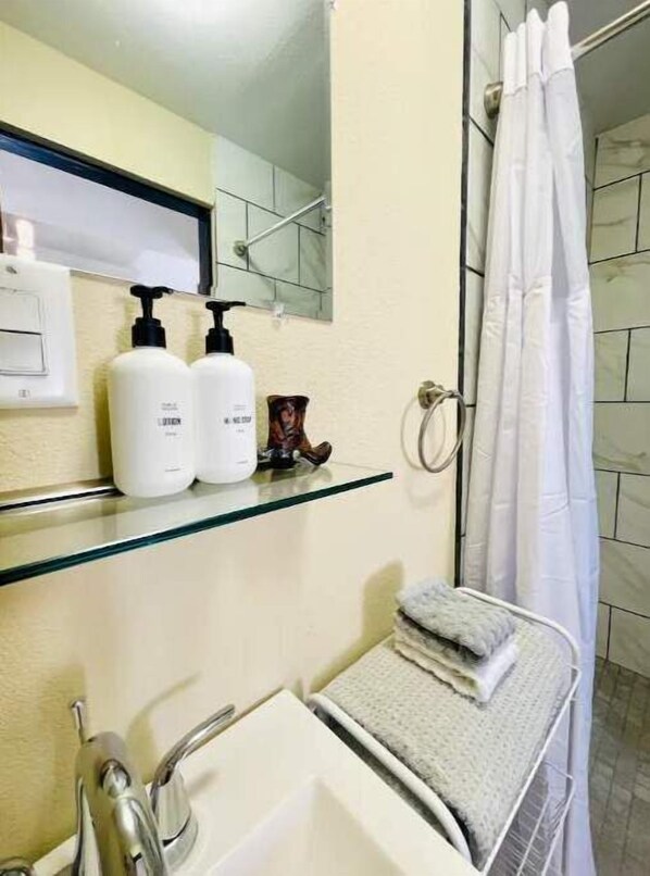 Une salle de bain avec une étagère en verre où sont rangés les articles de toilette, un lavabo et un rideau de douche.