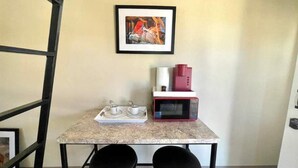 A small kitchen area with a marble countertop, two black stools, a framed picture on the wall, a microwave, and a coffee maker. - Vibes Cowboy: Three (Marfa)