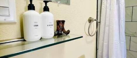 A bathroom with a glass shelf holding toiletries, a sink, and a shower curtain.