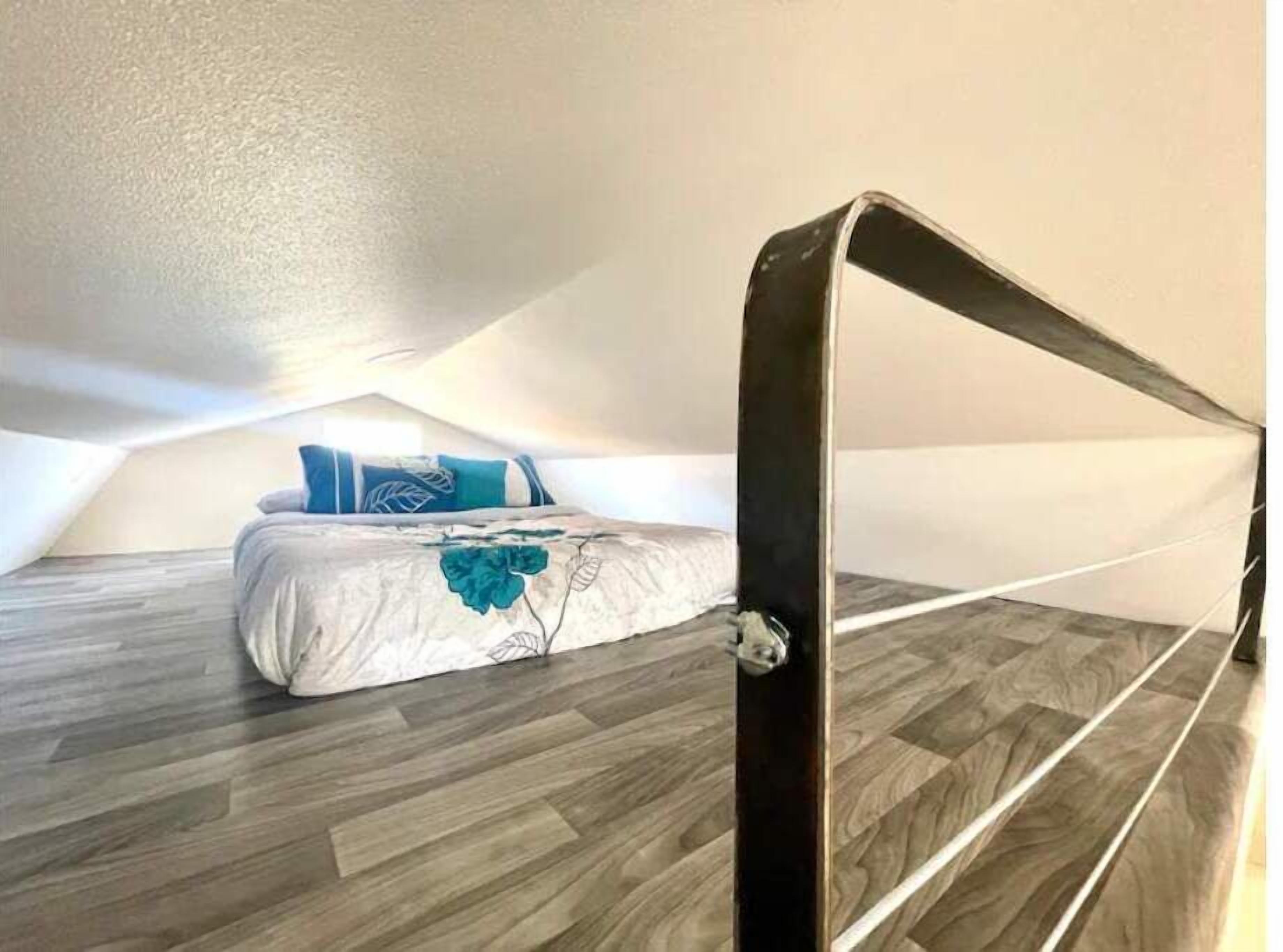 A bedroom with a sloped ceiling, a bed with a blue pillow, and a wooden floor.