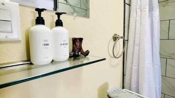 A bathroom with a glass shelf holding toiletries, a sink, and a shower curtain.