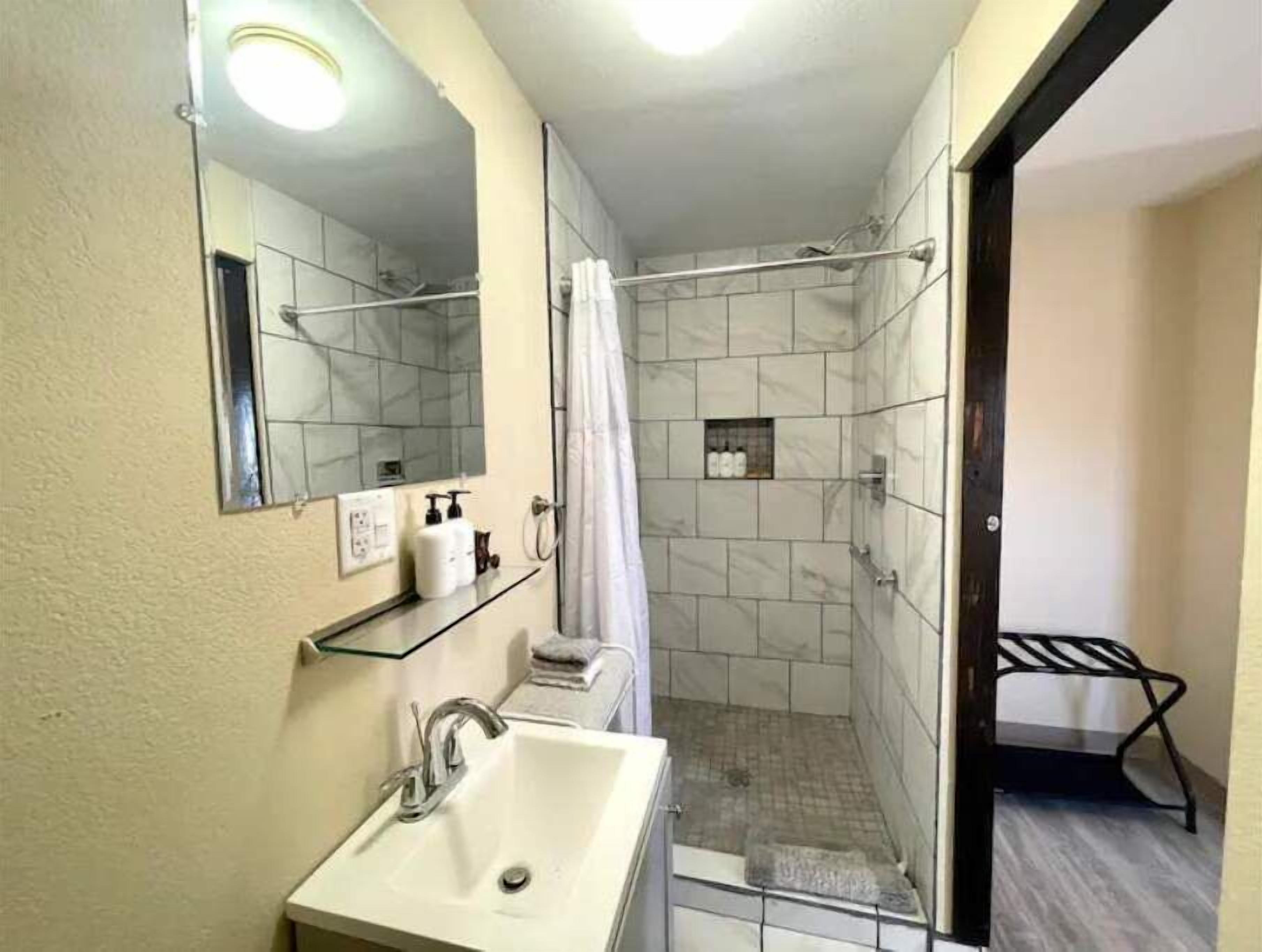A bathroom with a sink, mirror, shower, and a towel rack.