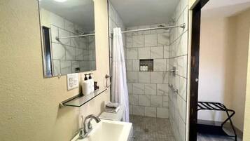 A bathroom with a sink, mirror, shower, and a towel rack.