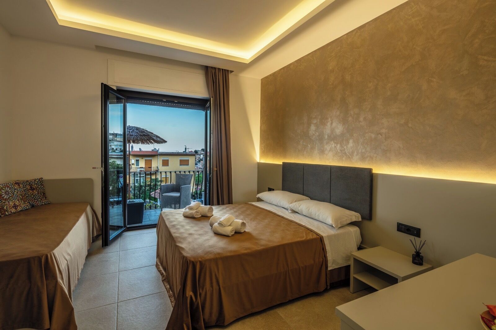 A hotel room with a bed, a desk, a chair, a balcony with a view, and a ceiling light.