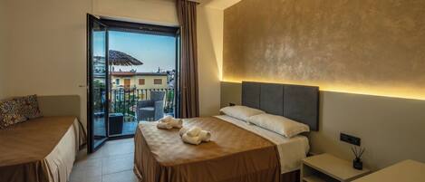 Habitación de hotel con cama, escritorio, silla, balcón con vistas y una lámpara en el techo.