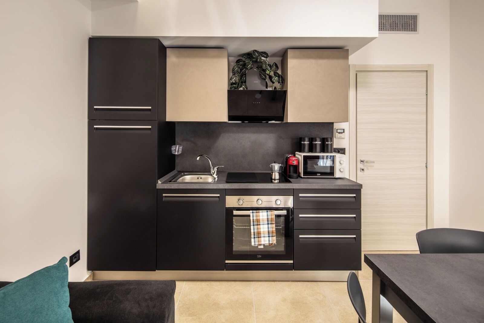Een praktische keuken met een ingebouwde oven, magnetron en koffiezetapparaat, een spoelbak en een klein raam boven het aanrecht.