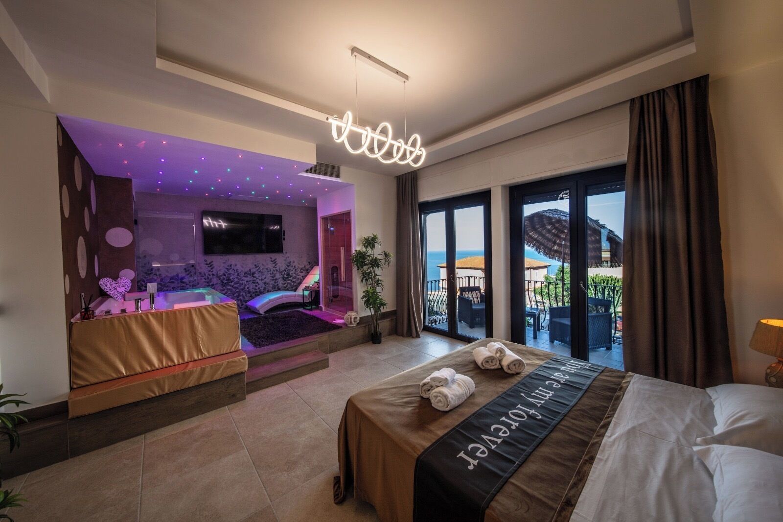 Habitación de hotel con cama, zona de masajes, televisor y balcón con vistas.