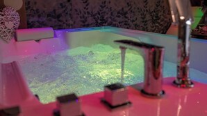 Une baignoire équipée de jets d’eau, un mur décoratif et une petite étagère avec quelques objets.