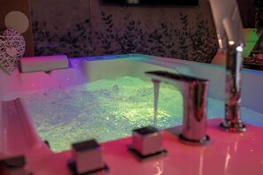 A bathtub with a water jet, a decorative wall, and a small shelf with items. - SUITE APARTMENT TAORMINA (Taormina)