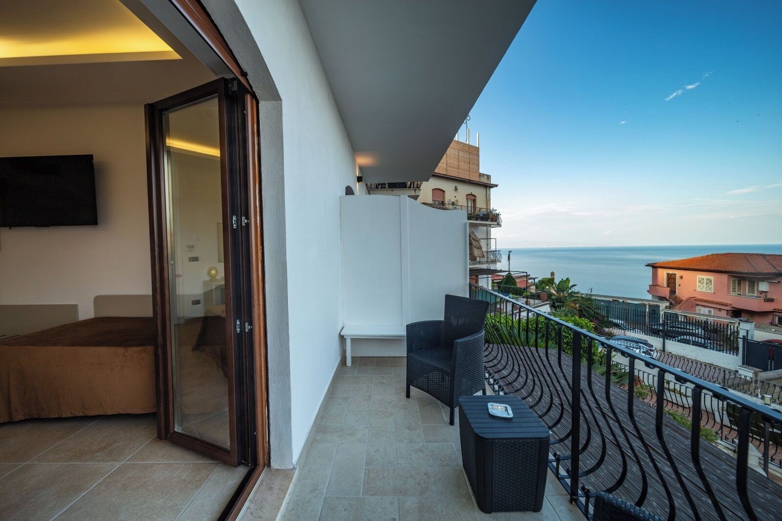 Un balcón con vista al mar, un sofá y un televisor montado en la pared.