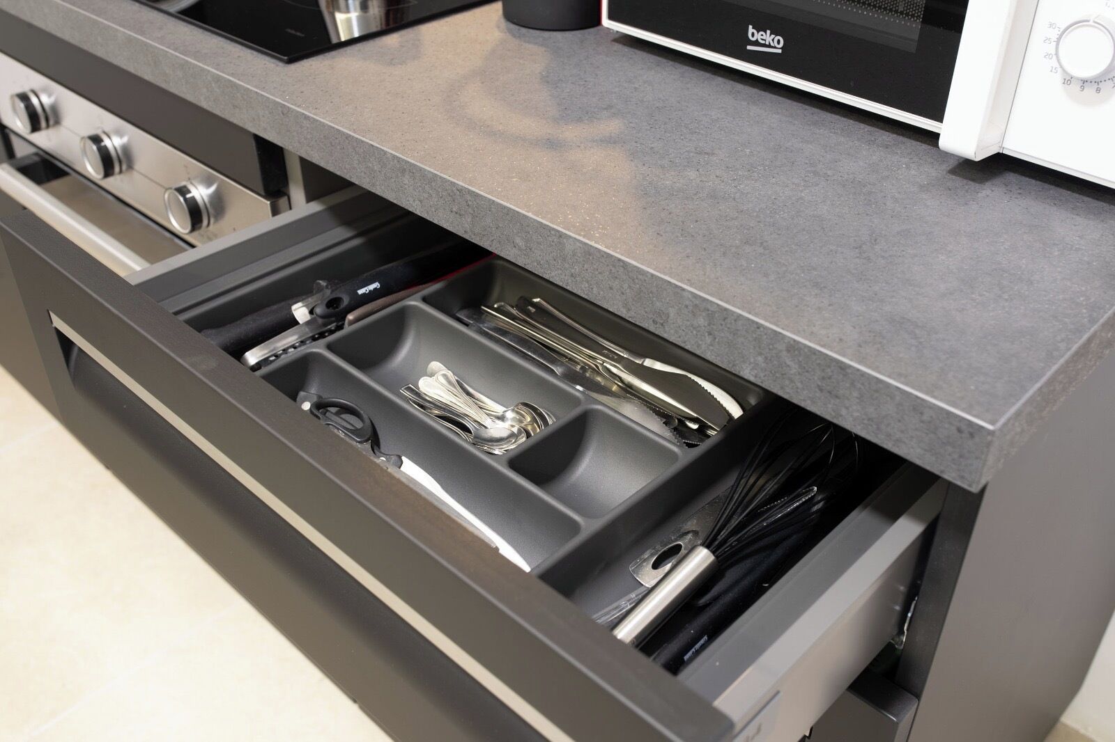 A kitchen with a built-in microwave, a stove, and a drawer with utensils.
