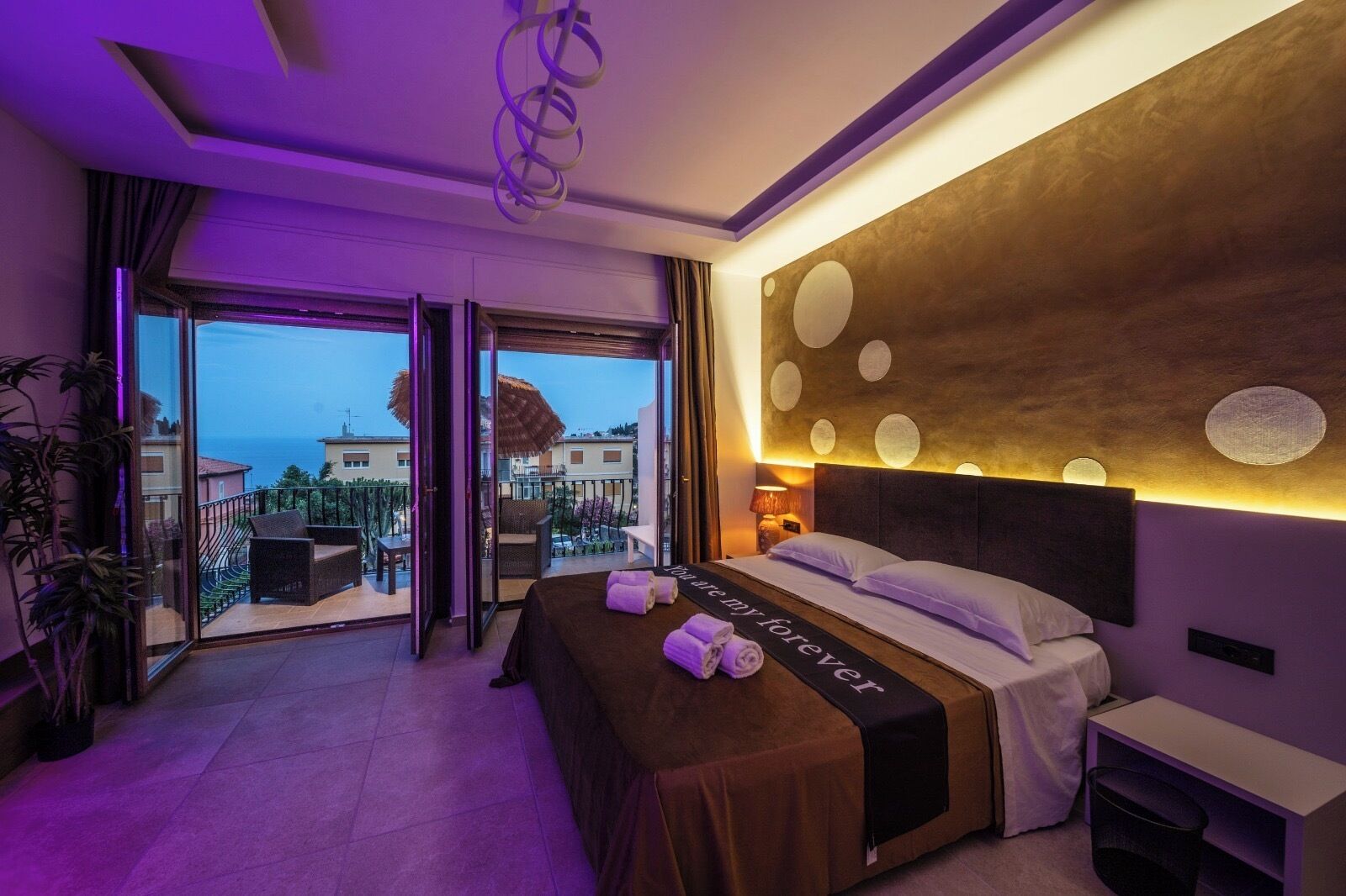 A hotel room with a balcony, a bed with a black bedspread, and a wall with circular patterns.