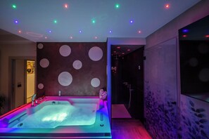 A modern spa room with a large hot tub, colorful ceiling lights, and a wall with circular patterns. - SUITE APARTMENT TAORMINA (Taormina)