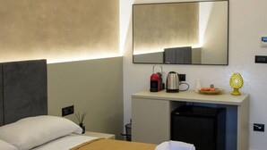 A hotel room with a bed, a desk with a kettle, a lamp, and a mirror.