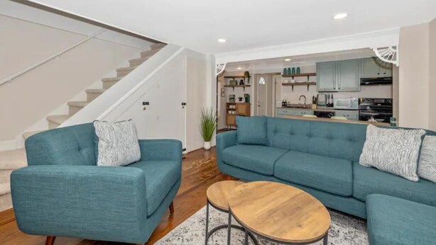 A modern living room with teal sofas and a wooden coffee table, a kitchen in the background, and a staircase leading to another level. - Unique Little Charmer in Downtown Frederick

 (Frederick)