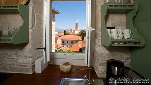 Une cuisine avec vue sur la ville, des murs en pierre et une fenêtre donnant sur des immeubles et une tour.