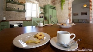 Une cuisine rustique aux murs en pierre, aux armoires vertes et à la table en bois, sur laquelle on peut voir des assiettes remplies de nourriture et une tasse.