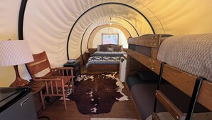 A cozy tented room with a bed, a chair, a desk with a lamp, and a rug.
