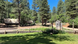 A rustic campsite with covered wooden structures, a wooden fence, and a dirt path.