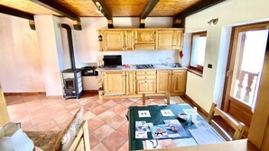 A kitchen with wooden cabinets, a stove, and a dining area with a table set for two. - Rilassante Baita con Giardino Recintato (Gignod)