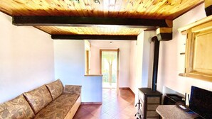 A cozy living room with a wooden ceiling, a sofa, a television, and a kitchen area with a stove. - Rilassante Baita con Giardino Recintato (Gignod)