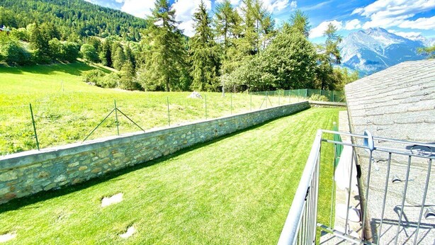 A stone wall with a metal railing, a grassy area, and a mountainous landscape in the background. - Rilassante Baita con Giardino Recintato (Gignod)