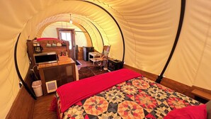 Um quarto acolhedor com tenda, uma cama, uma escrivaninha com computador, uma cadeira e uma pequena mesa.