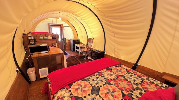 A cozy tented room with a bed, a desk with a computer, a chair, and a small table.