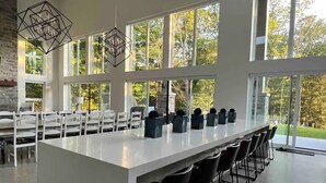 A modern bar area with a long counter, multiple chairs, and large windows offering a view of the outdoors. - Muskoka Modern Luxury Lake House Cottage (Port Carling)
