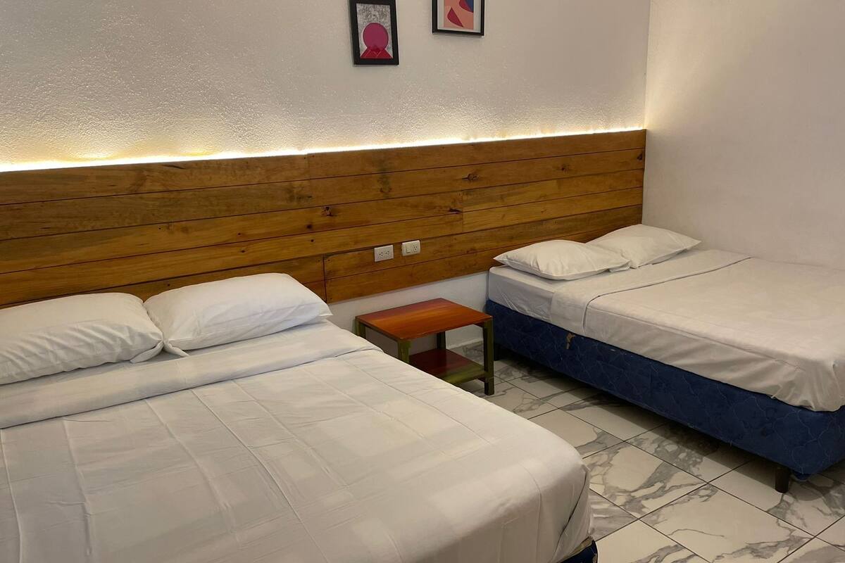 Habitación de hotel con dos camas, cabecera de madera, pequeño banco de madera y suelo de baldosas de mármol.