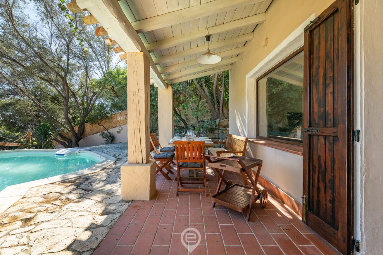 Un patio techado al aire libre con piscina, muebles de madera y suelo de baldosas de piedra.