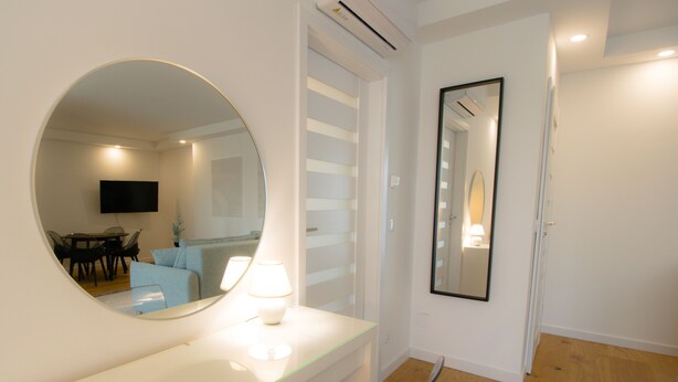 Un baño moderno con un espejo redondo, un tocador blanco y suelo de madera.