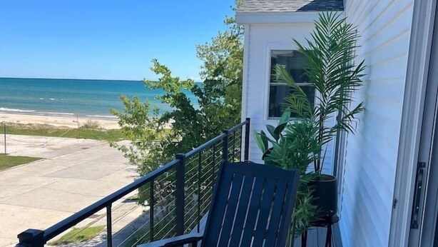 A balcony with a rocking chair and a small round table, overlooking a beach.
