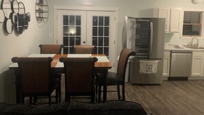 A dining area with a wooden table and chairs, a kitchen with white cabinets and appliances, and a hallway with a door. - Cozy Lake House near Pymatuning Lake (Jamestown)