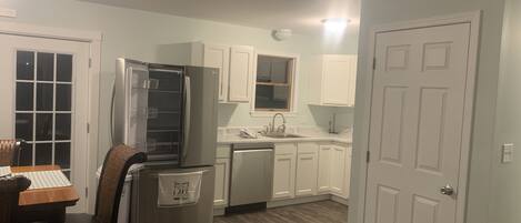 Cocina compacta con armarios blancos, un refrigerador de acero inoxidable, lavavajillas y un comedor con mesa y sillas.