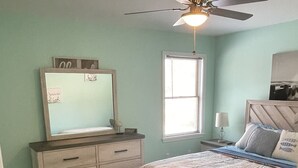A bedroom with a bed, dresser, mirror, ceiling fan, window, and nightstand. - Cozy Lake House near Pymatuning Lake (Jamestown)